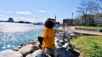 Woman sitting on rocks along the bank of a harbor in Baltimore Maryland
