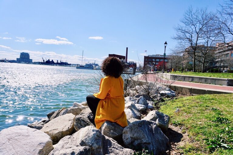 Woman sitting on rocks along the bank of a harbor in Baltimore Maryland