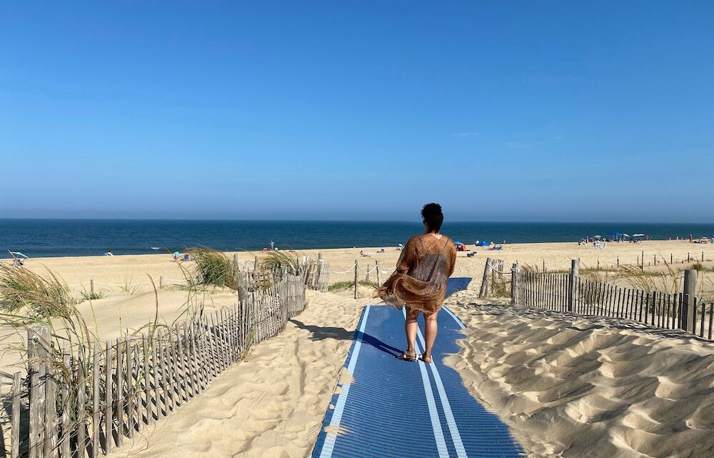 Woman walking on pathway between sand dunes to the beach in Delaware