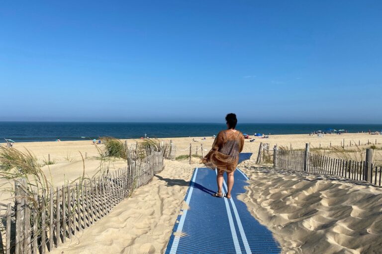 Woman walking on pathway between sand dunes to the beach in Delaware