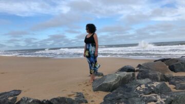 woman stands on a beach with rocks on the sand and crashing waves