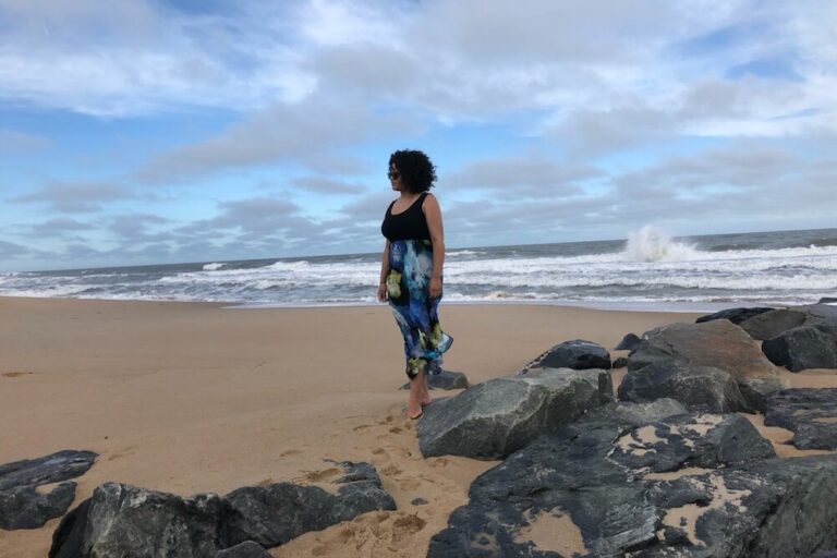 woman stands on a beach with rocks on the sand and crashing waves