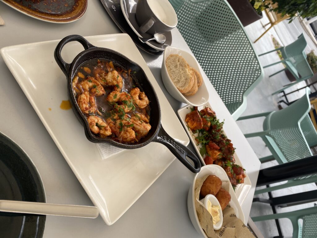 Skillet of grilled garlic shrimp, plate of patatas bravas, and plate of croquettes on a table in Spain