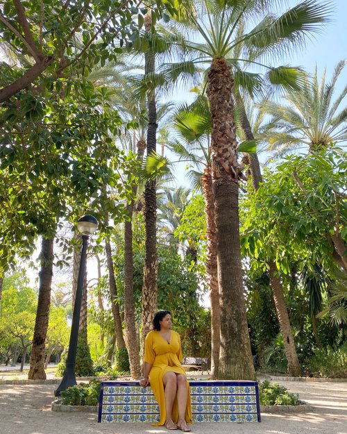 Woman in a yellow dress sitting on a tiled bench with palm trees in the background in Elche Spain.