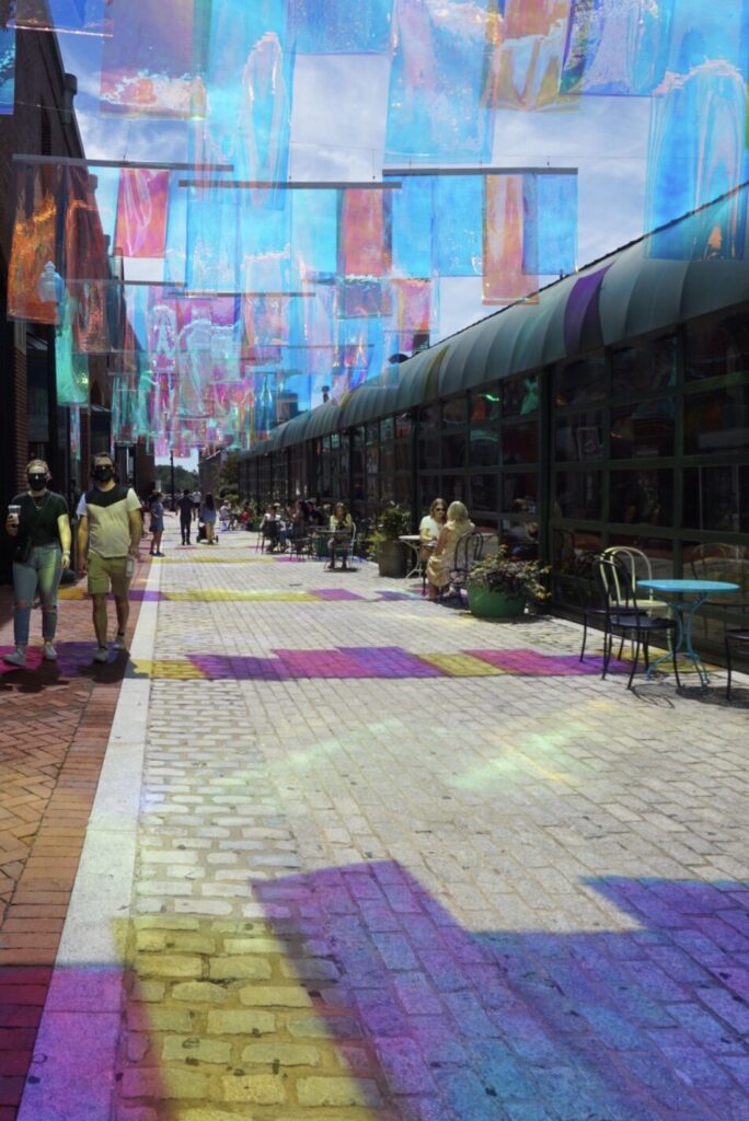 A cobblestone street in Georgetown Washington DC with colored translucent streamers hung up and reflecting on the ground