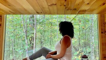 Woman sitting on bed in front of large window in tiny cabin