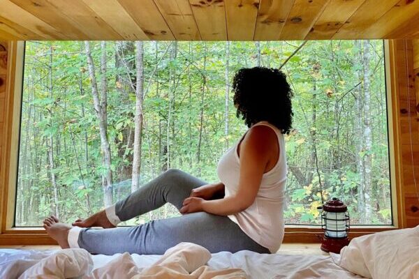 Woman sitting on bed in front of large window in tiny cabin