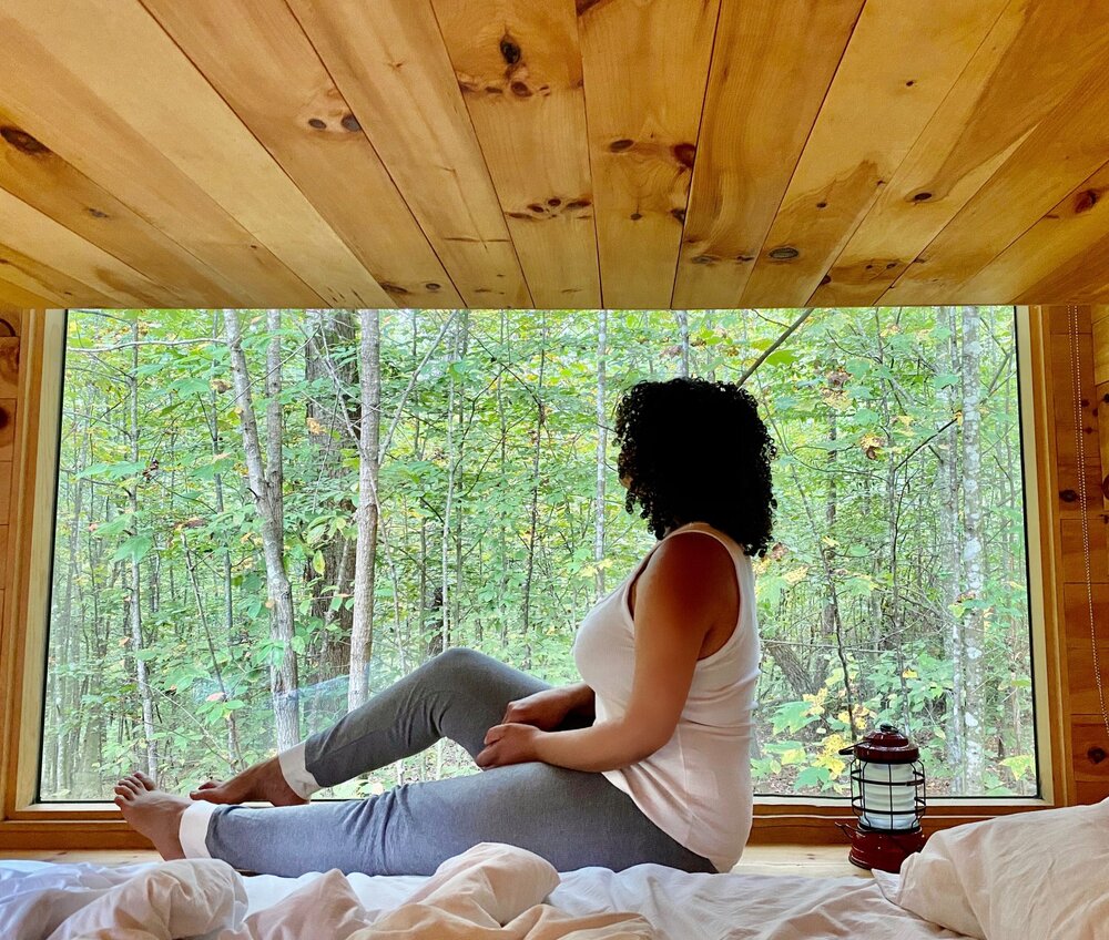 Woman sitting on bed in front of large window in tiny cabin