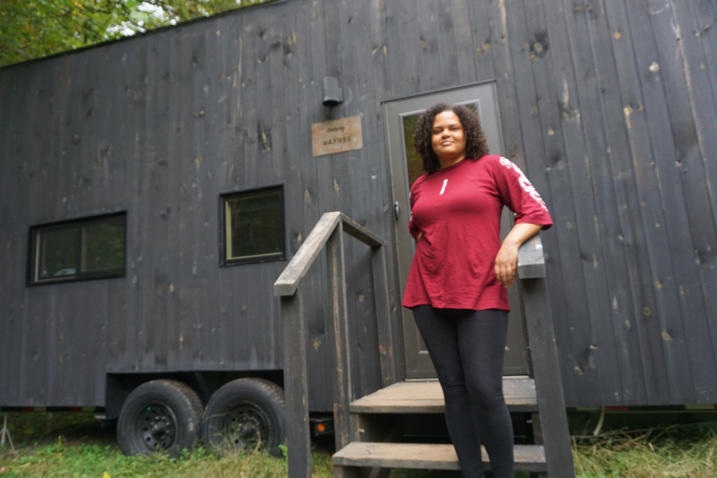 Woman standing on the steps outside of a wooden tiny cabin in the woods