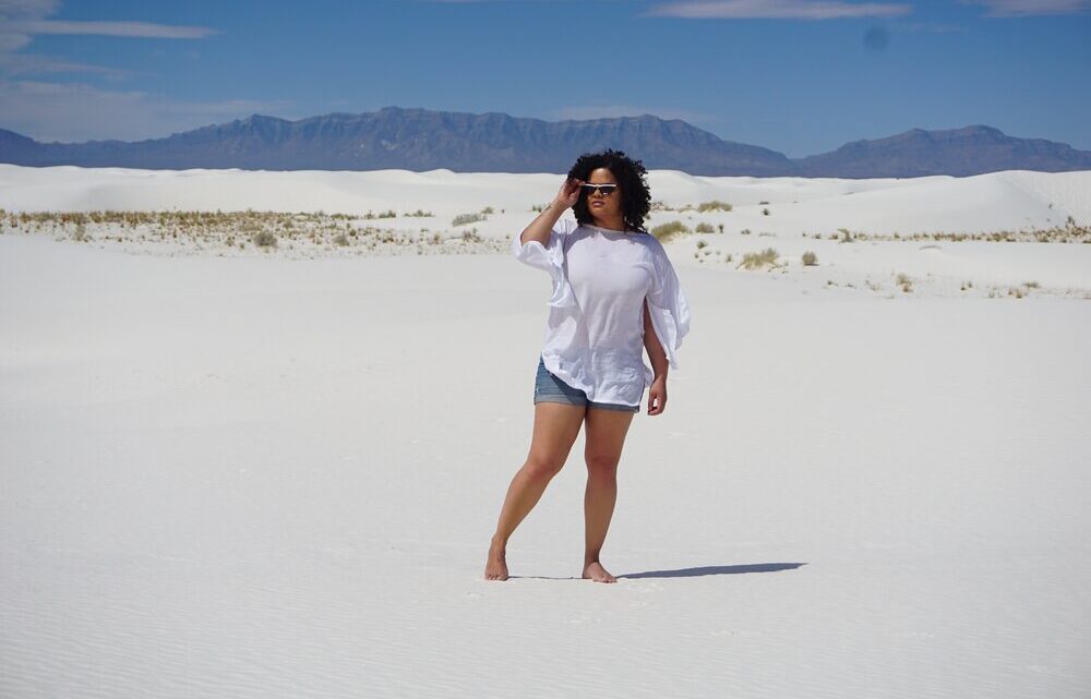 Woman standing on a white sand dune with mountains in the background