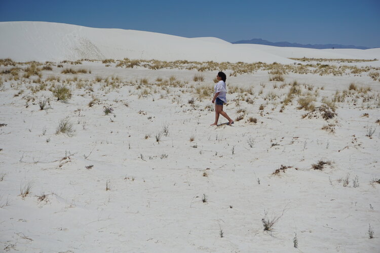 Woman walking across landscape of white gypsum sand dunes in New Mexico