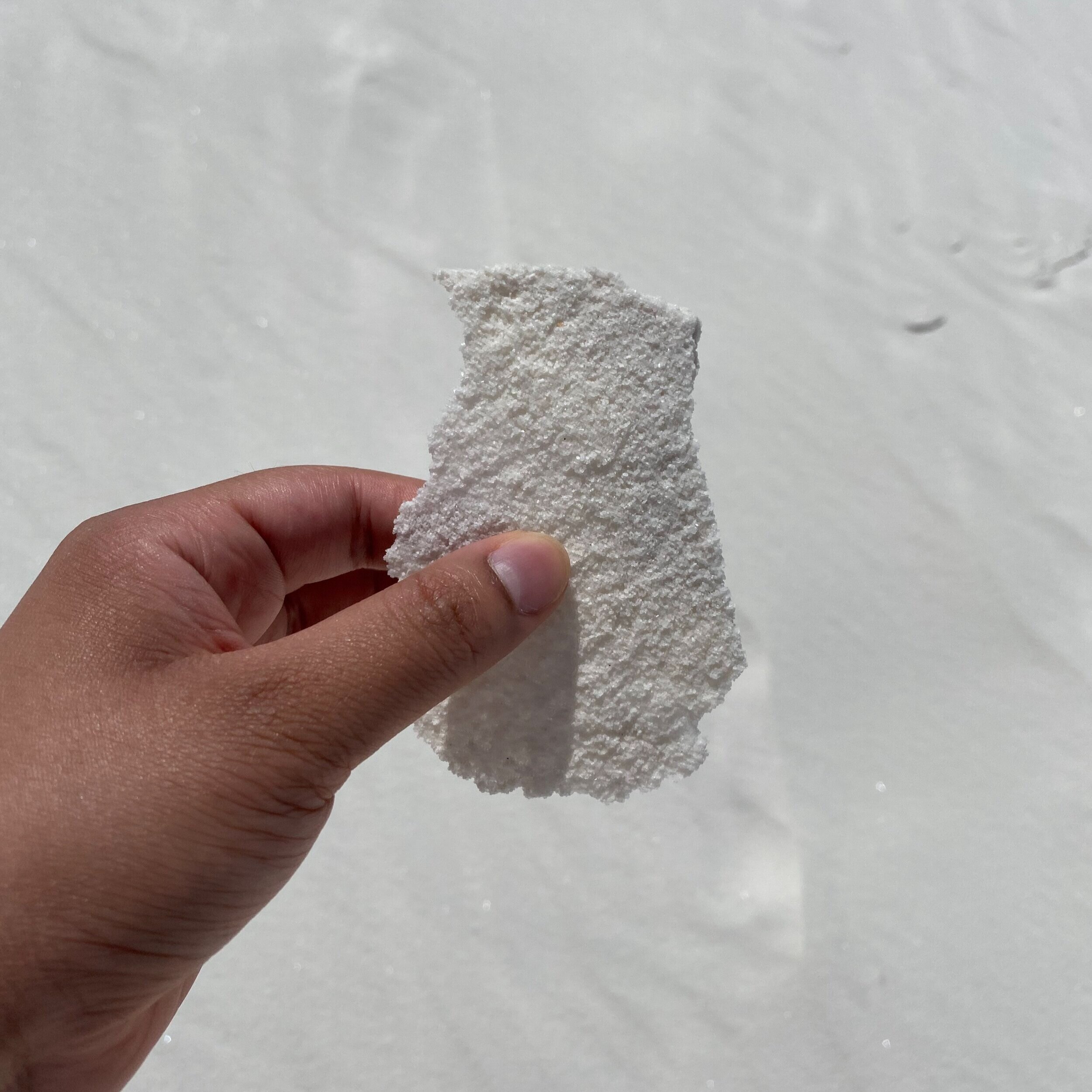 A hand holding up a piece of hardened white gypsum sand in New Mexico