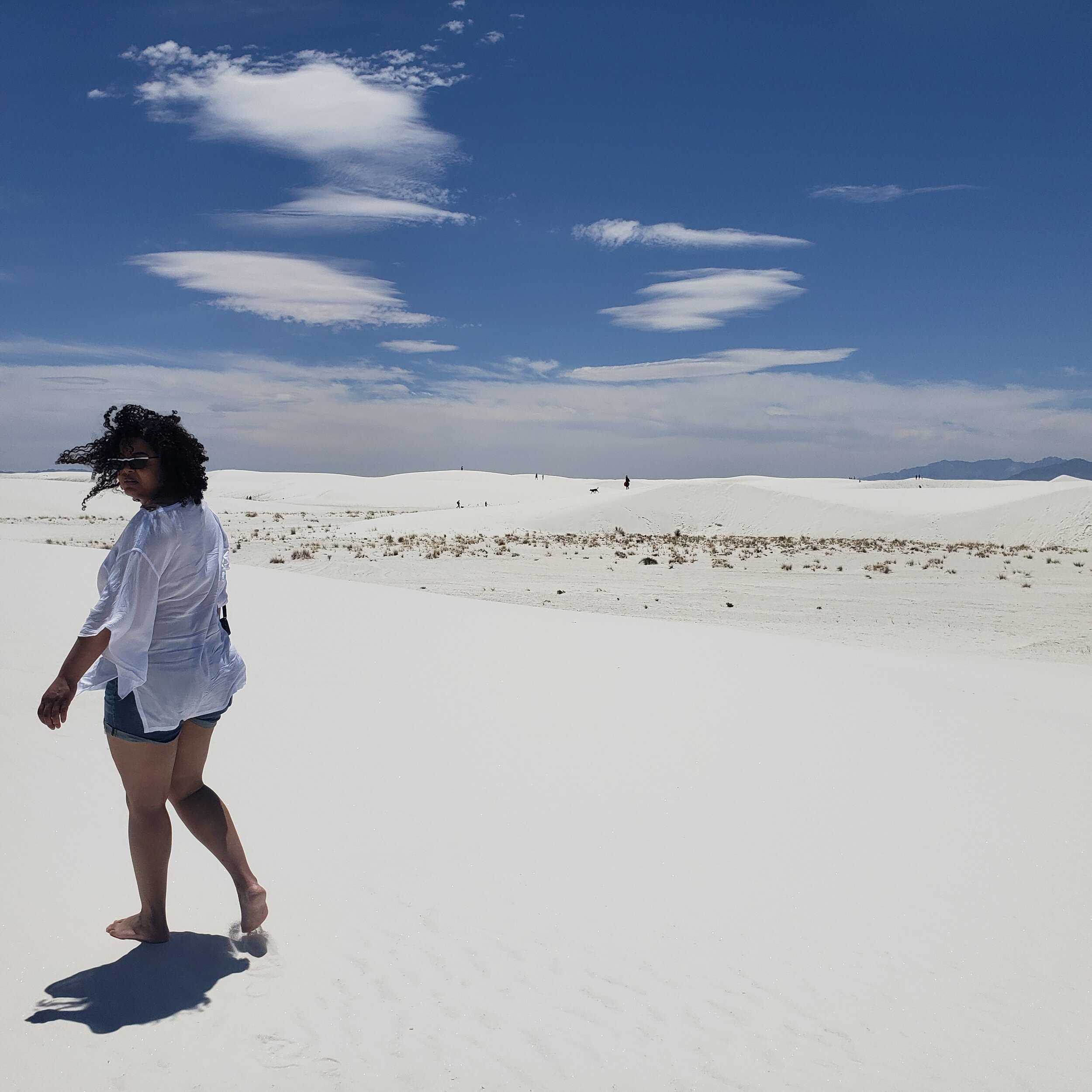 Woman walking along white sand dunes with open blue sky in New Mexico
