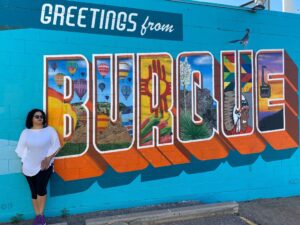 Woman leaning against street mural that says Greetings from Burque in Albuquerque New Mexico