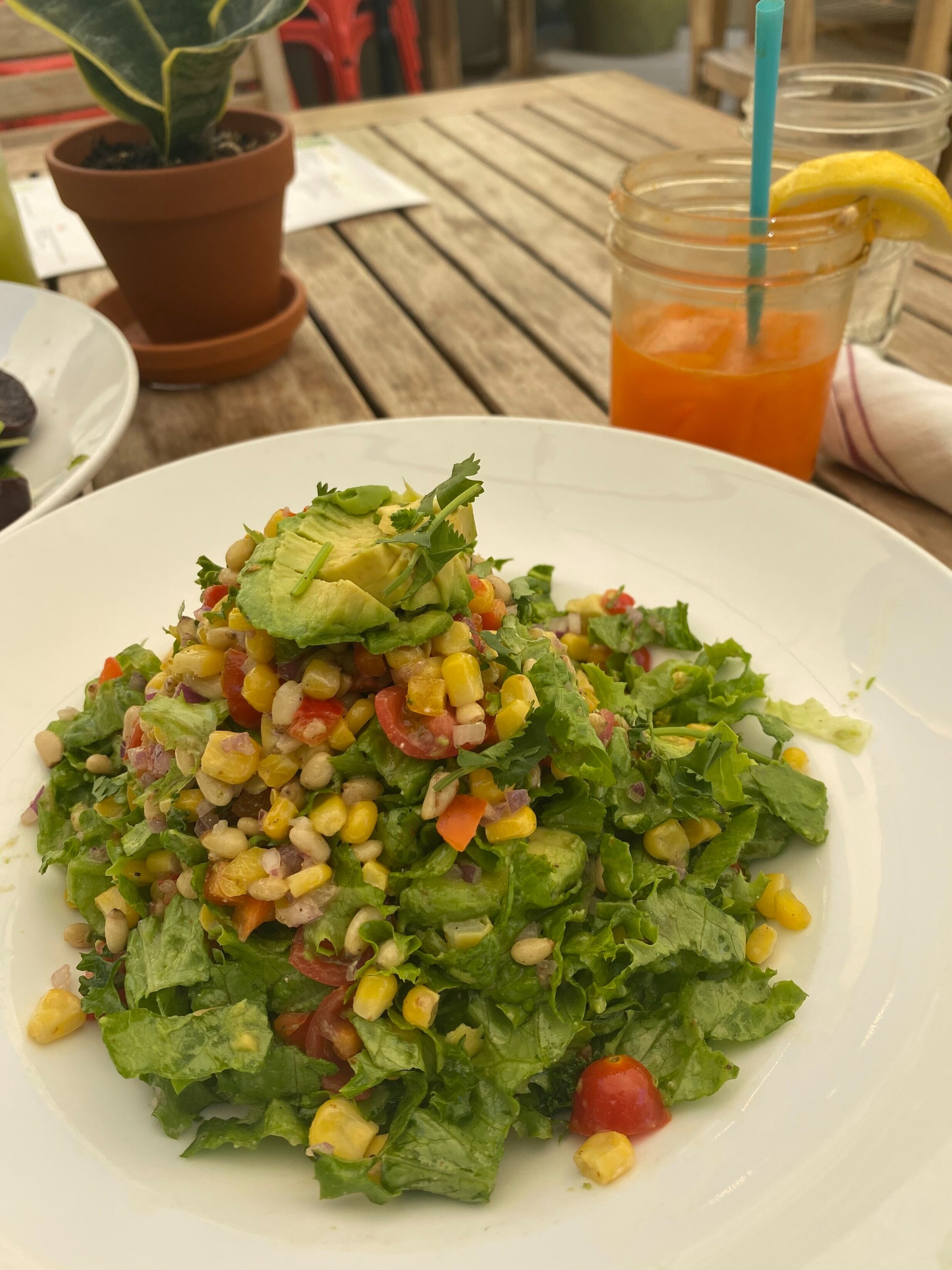 Plate of salad with corn and avocado and a Mason jar of fruit and vegetable juice on an outdoor restaurant table