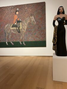 Statue of a woman on a museum display stand in front of a painting of a man on a horse.