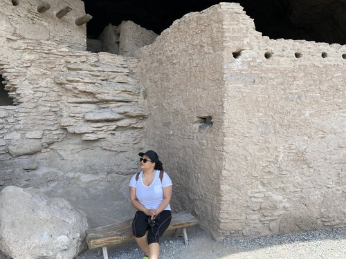Woman sitting on bench in front of cliff dwelling historic site in New Mexico