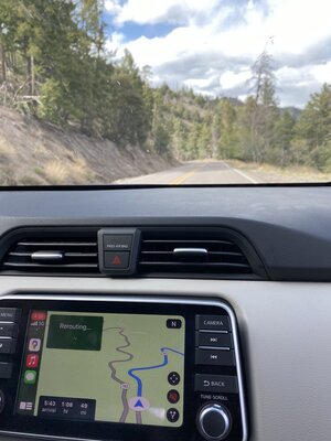 Car dashboard showing GPS of New Mexico winding road with the road, trees, and mountain through the windshield