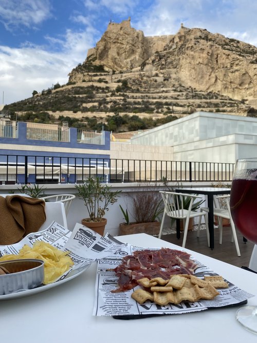 Plate of ham and crackers on a restaurant patio table overlooking a hilltop castle in Alicante Spain