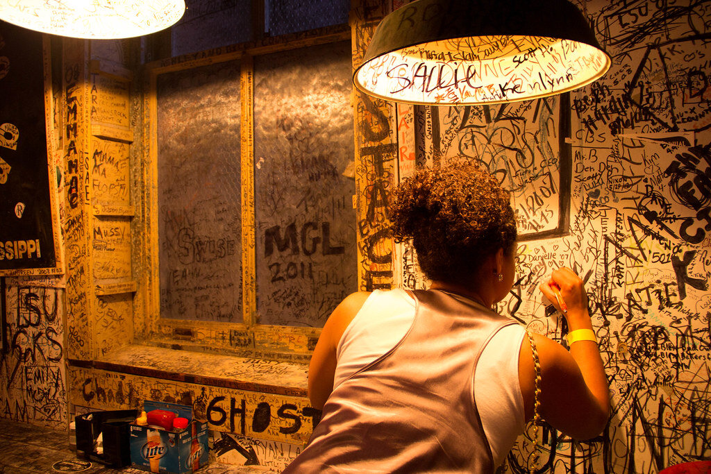 Woman writing on the wall of a bar, fully covered with signatures and graffiti.