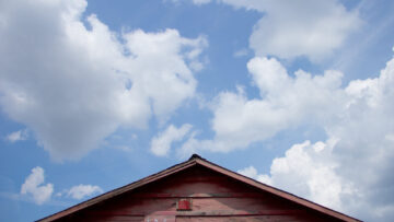 Top of wooden shotgun house with blue sky and clouds above it