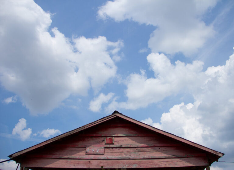 Top of wooden shotgun house with blue sky and clouds above it