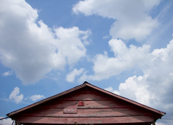 Top of wooden shotgun house with blue sky and clouds above it