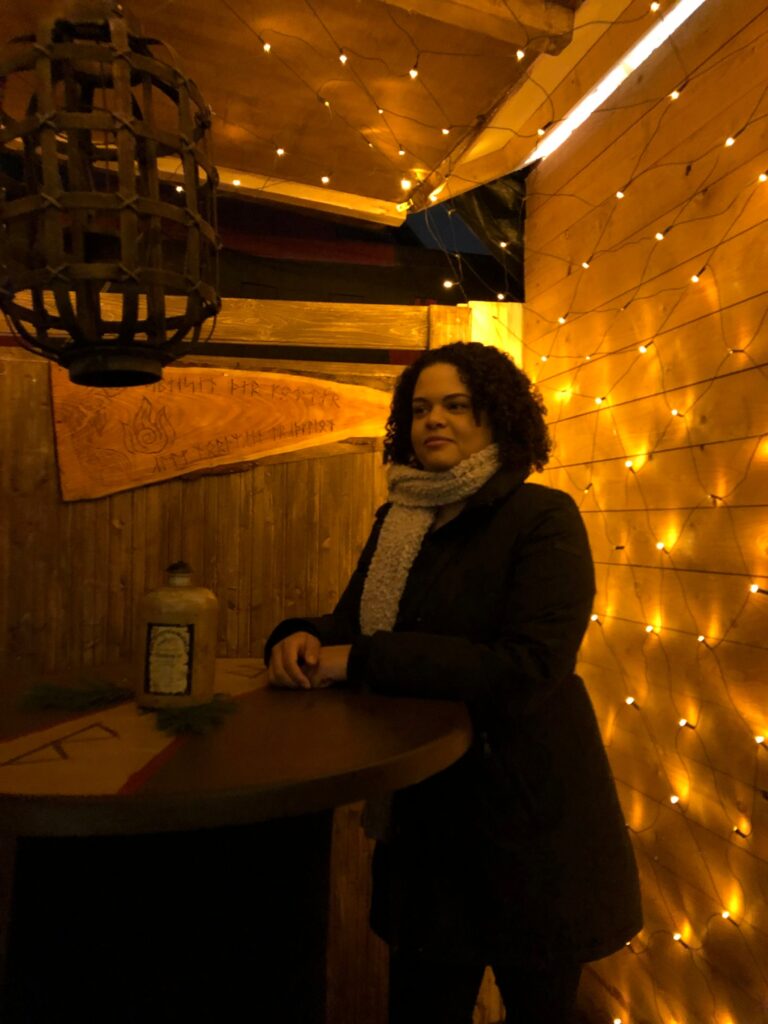 Woman at a standing table in a wooden booth with string lights on the wall behind her