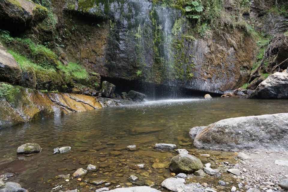 Large boulders and a wall of rock with a small waterfall and a pool of water below it