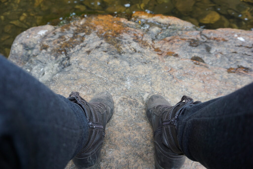 A pair of feet in boots standing on a rock surrounded by water in a Colombia forest