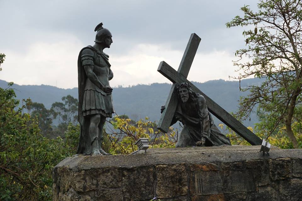 Sculpture of Jesus carrying the cross with trees and mountain range outline in the background