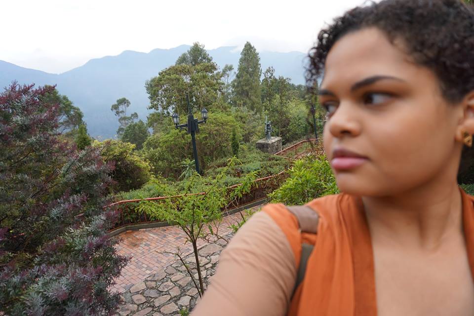 Woman taking a selfie with a stone path, trees, and mountain range outline in the background while exploring Bogotá Colombia