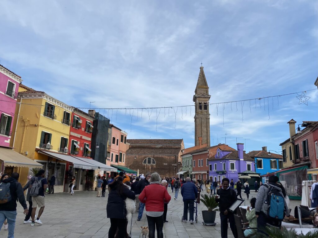 Burano town plaza with colorful homes and a tower in Venice Italy