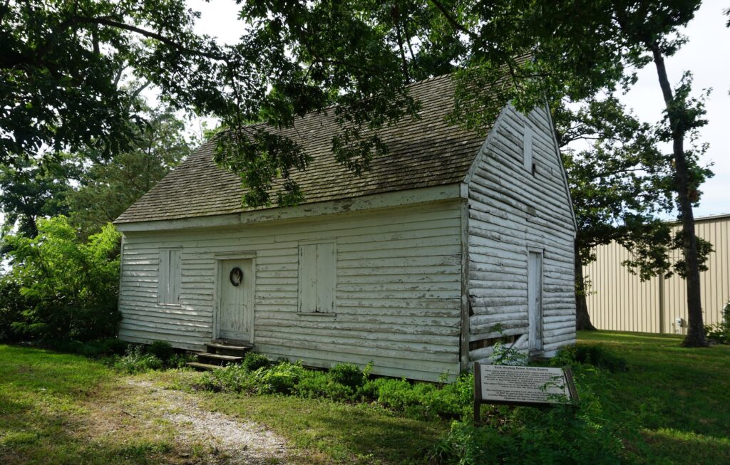 White historic one-room meeting house on a grassy field and under trees