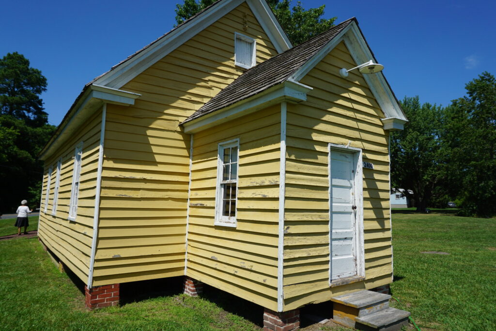 A historic yellow one-room schoolhouse in a grassy field
