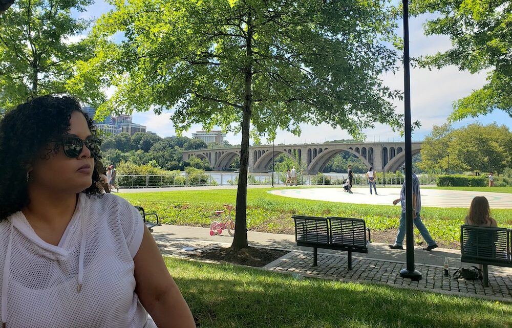Woman in forefront with Georgetown, Washington DC bridge, river, and park in the background