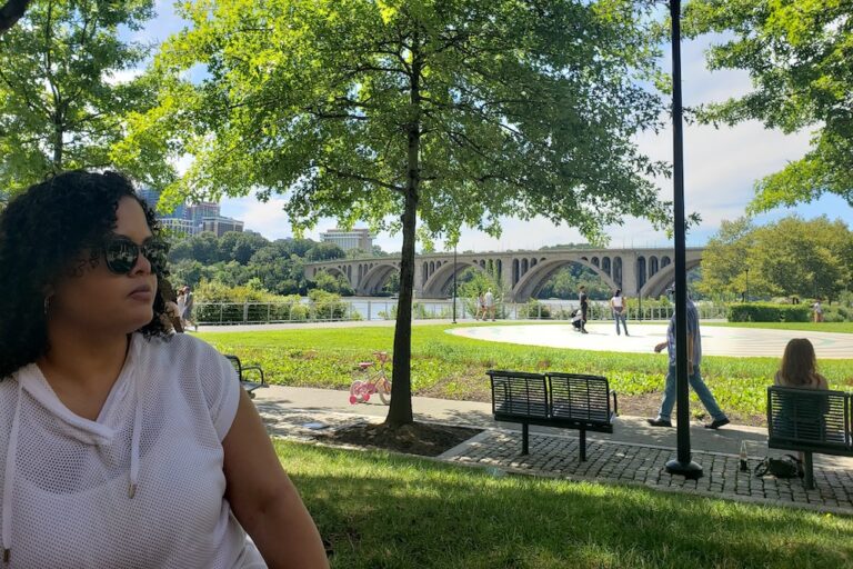 Woman in forefront with Georgetown, Washington DC bridge, river, and park in the background