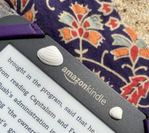 Close-up of an Amazon Kindle on a beach blanket with small shells laying on it in Fenwick Island Delaware