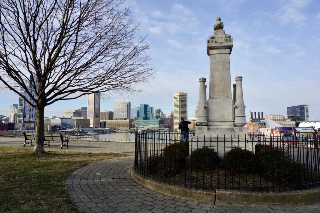Baltimore Maryland park with a statue, tree, and view of the city skyline