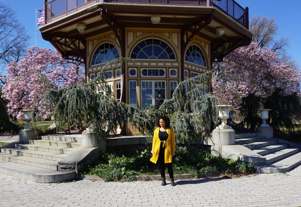 Woman in yellow jacket in front of a tall pagoda framed by pink magnolia trees in Baltimore Maryland