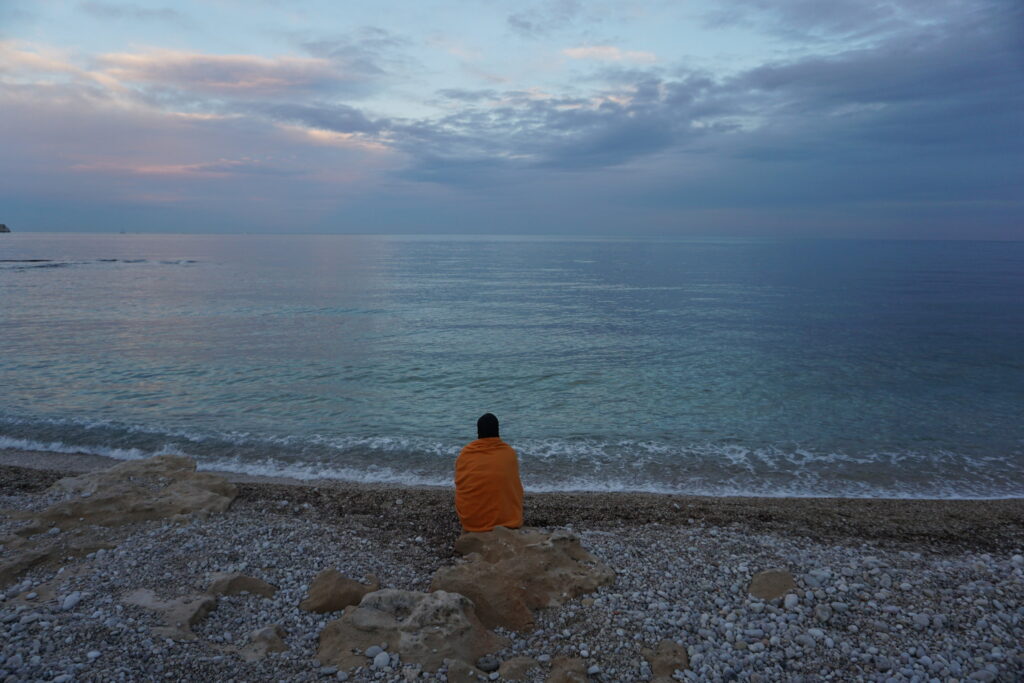 Woman in an orange shawl sitting on the beach watching a sunset over the Mediterranean