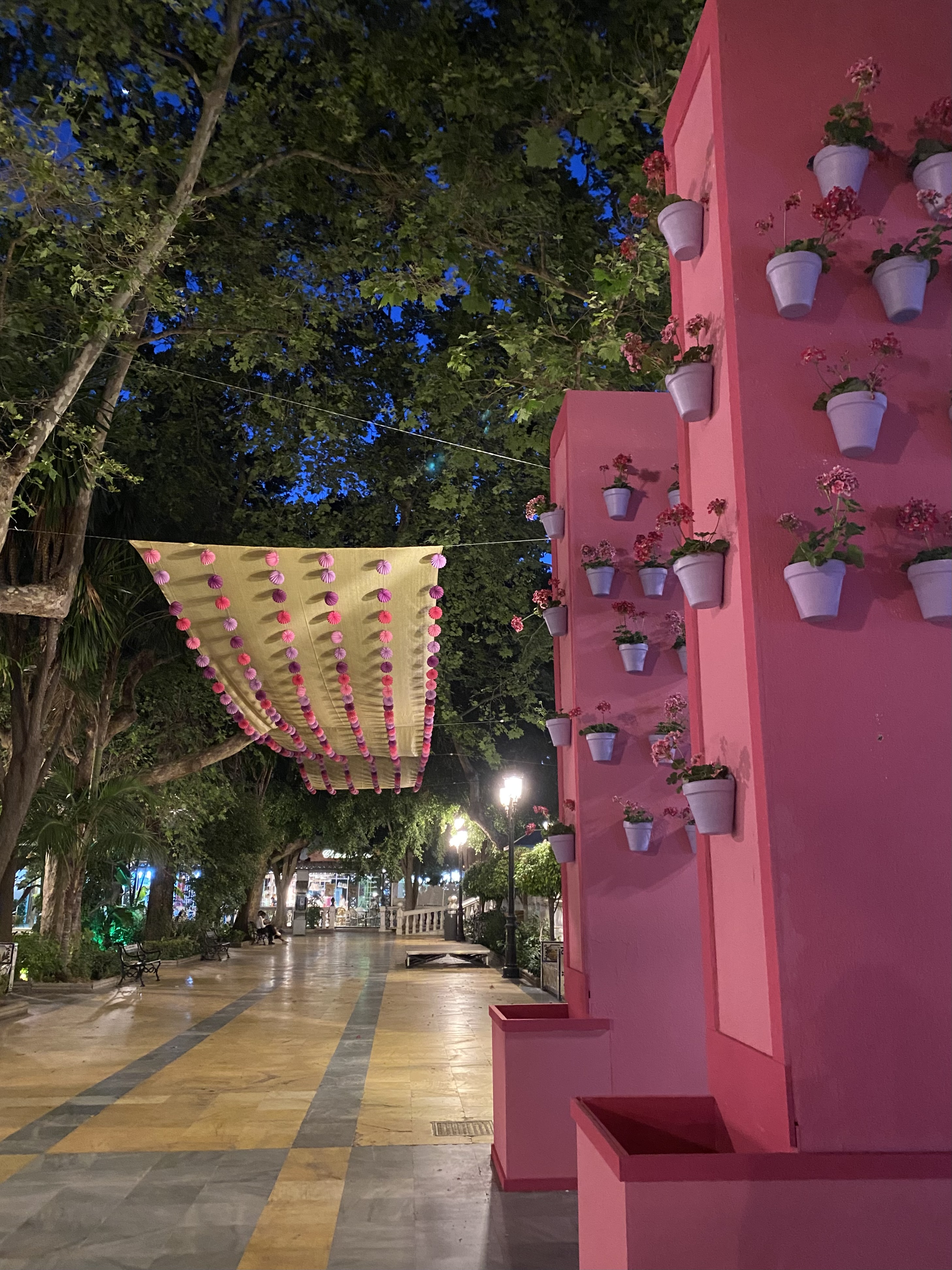 Pink pillars with potted flowers hanging on them and decorations in a Marbella park