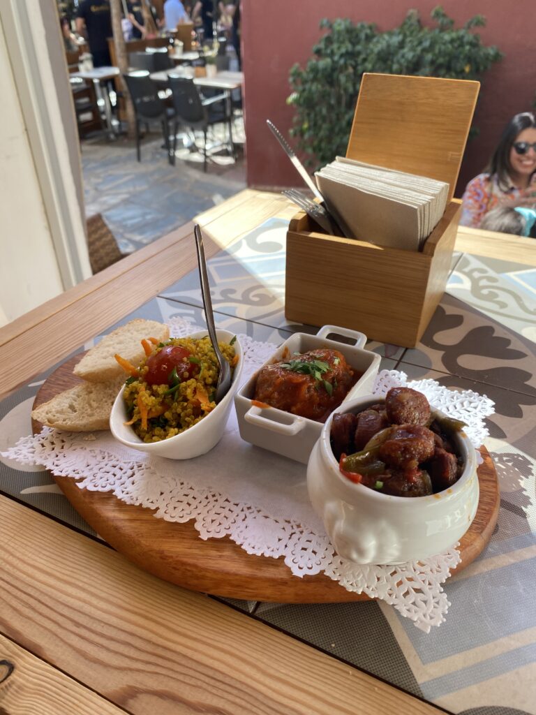 A wooden serving board with three tapas and bread on a cafe table