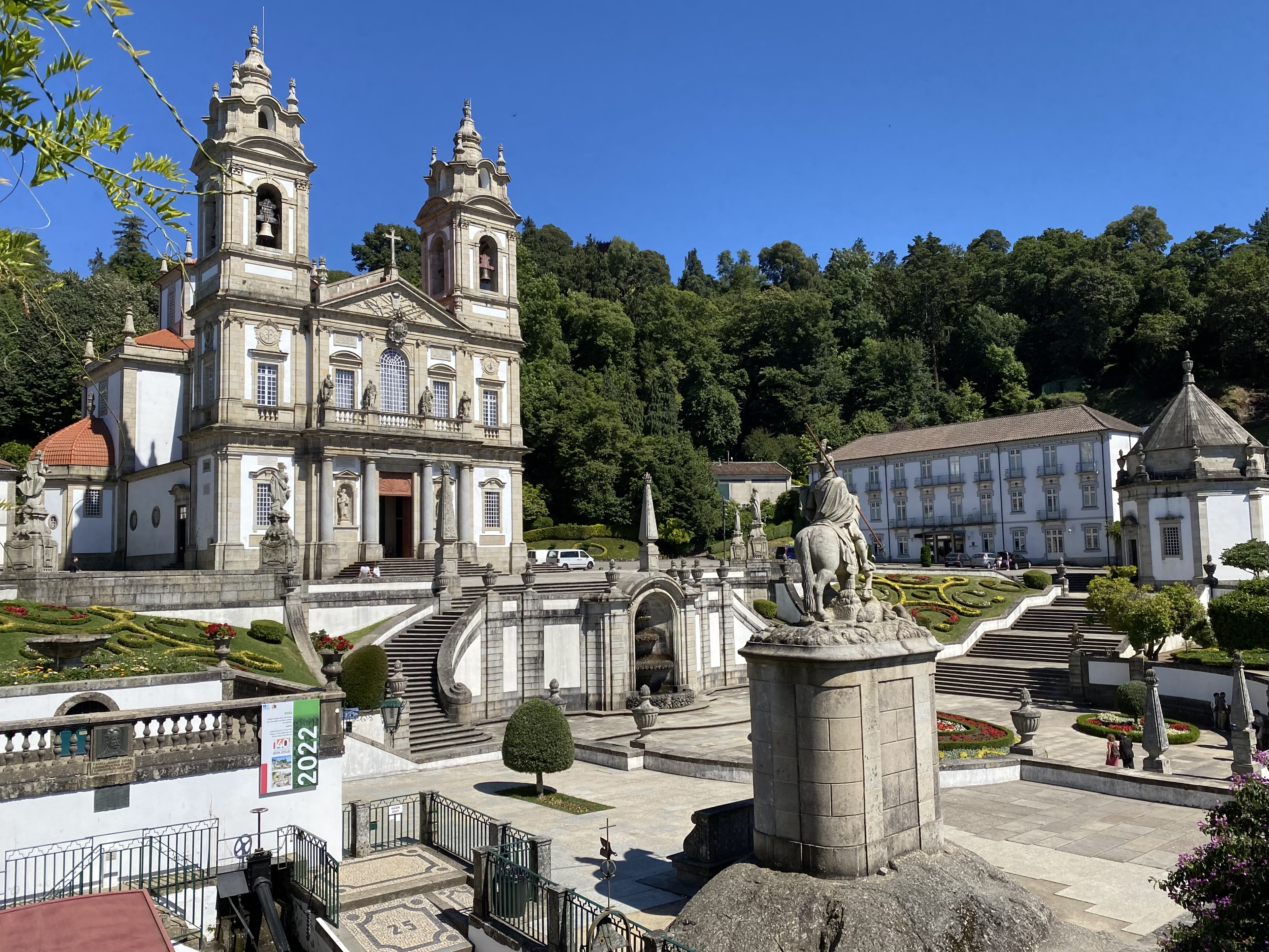 Catholic cathedral with plaza in front containing statues, manicured gardens, and steps