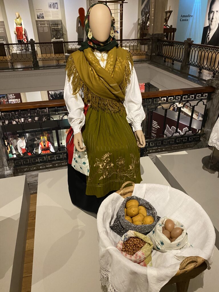Museum mannequin dressed in traditional northern Portugal blouse, skirt, gold filigree jewelry, and scarf with basket of produce in front of it