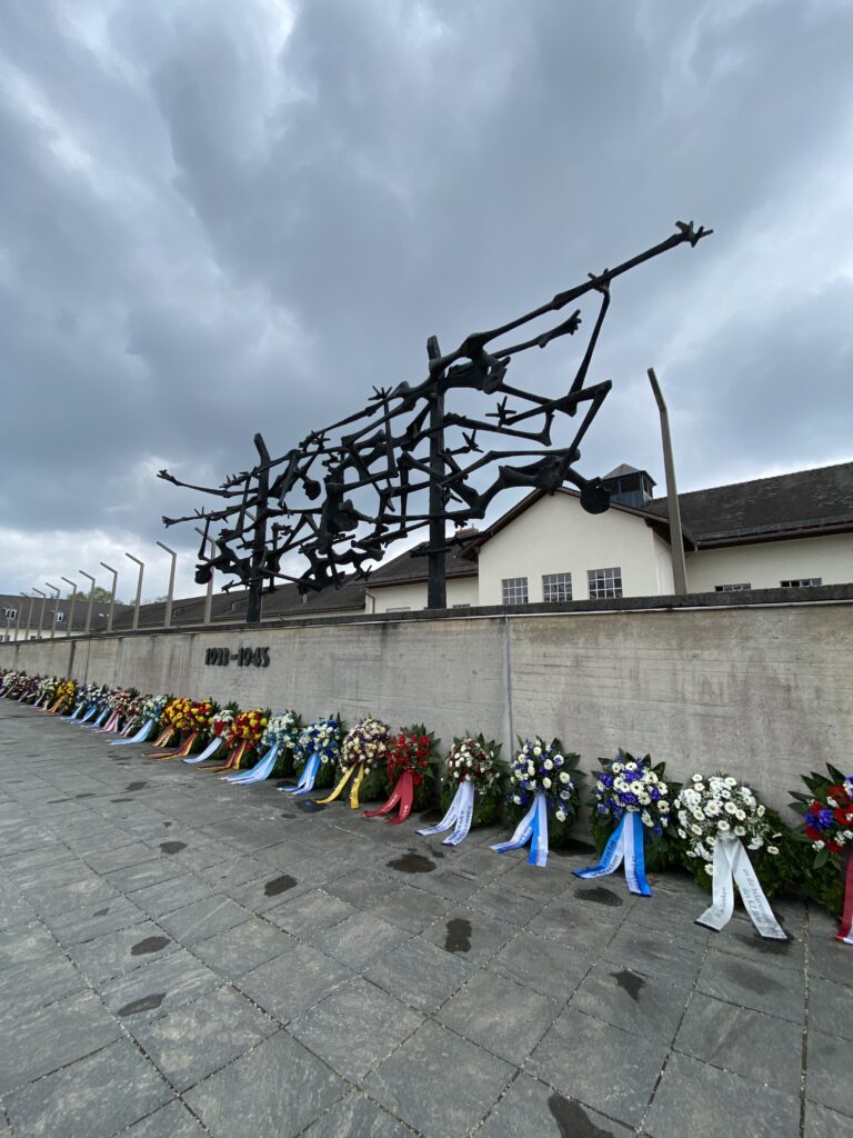 Holocaust memorial statue above wreaths laid along a low wall