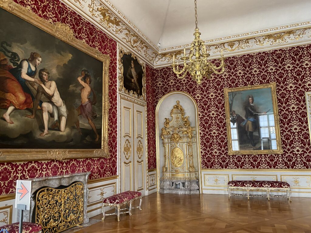 Munich palace room with red and gold walls, a large painting, and ornate benches