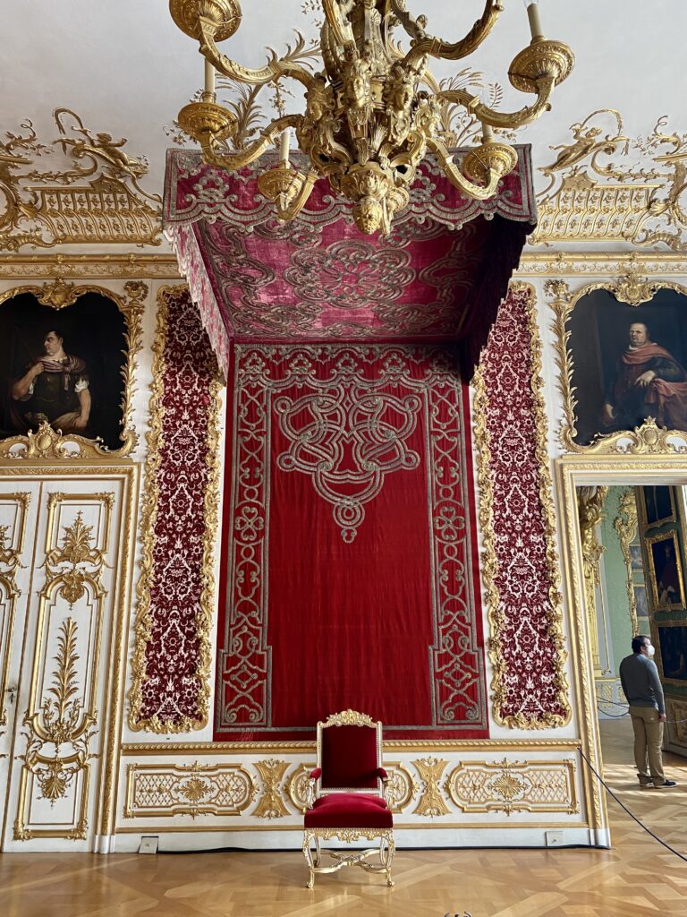 Royal red and gold chair in a Munich palace room under a red and gold canopy