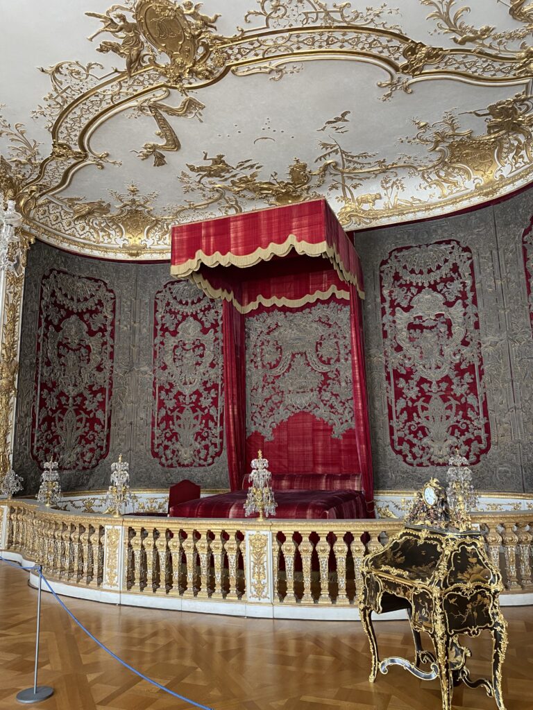 Munich palace bedroom with red and gold bed behind a small gate and gold ceiling details
