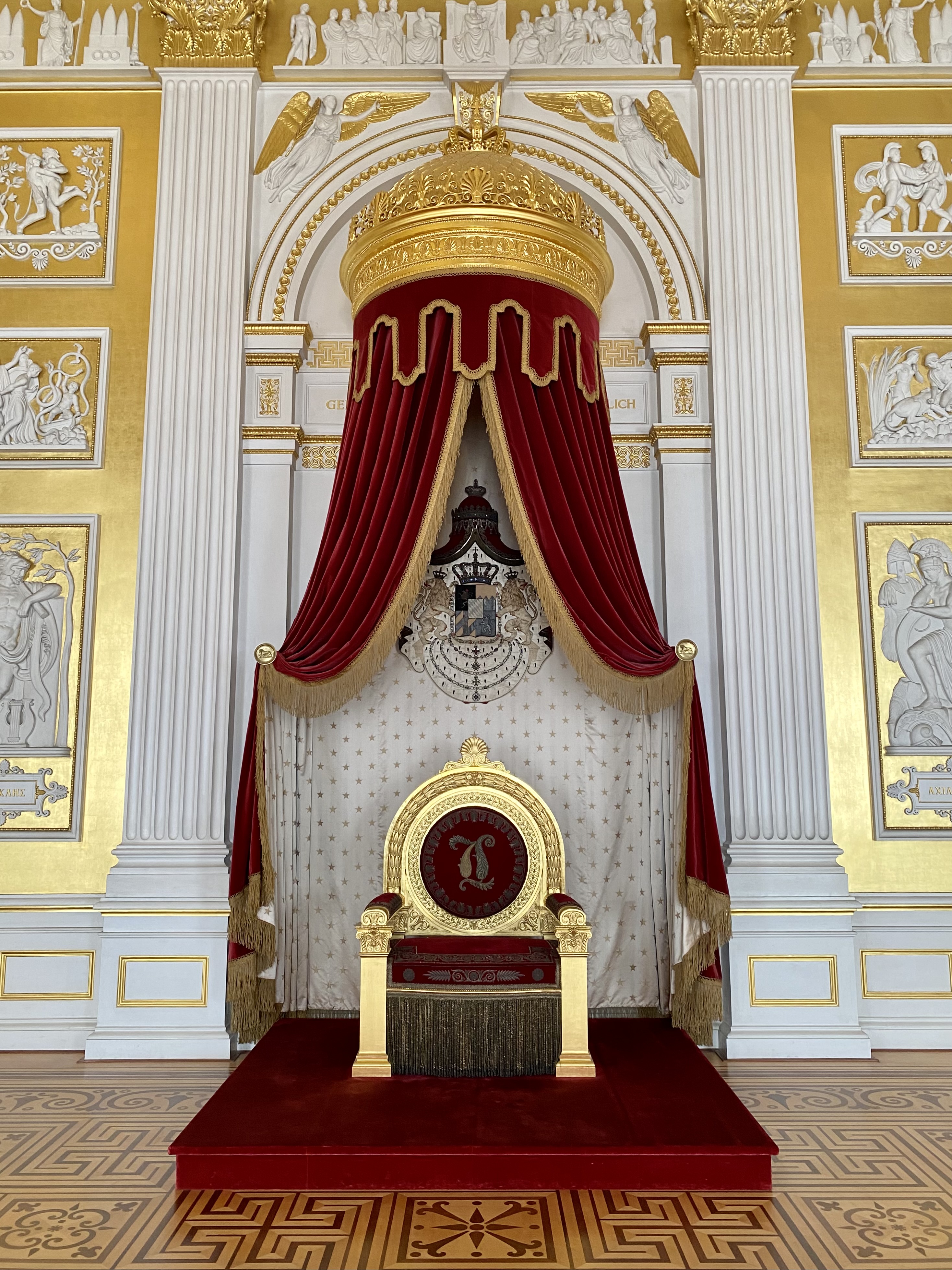 Red and gold royal chair on a platform under a red and gold canopy